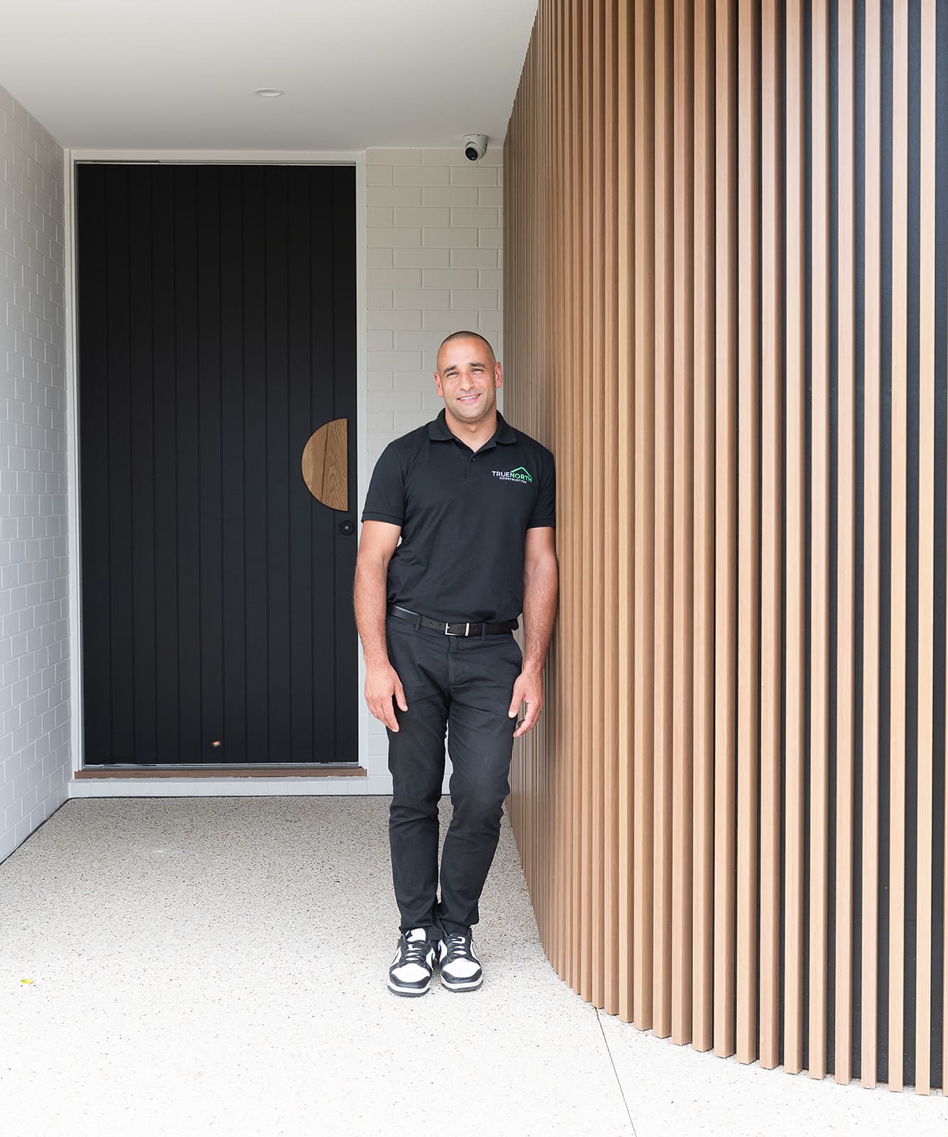 Omar of True North Construction at the entry of the Patricia residence, beside its black front door and curved timber battens