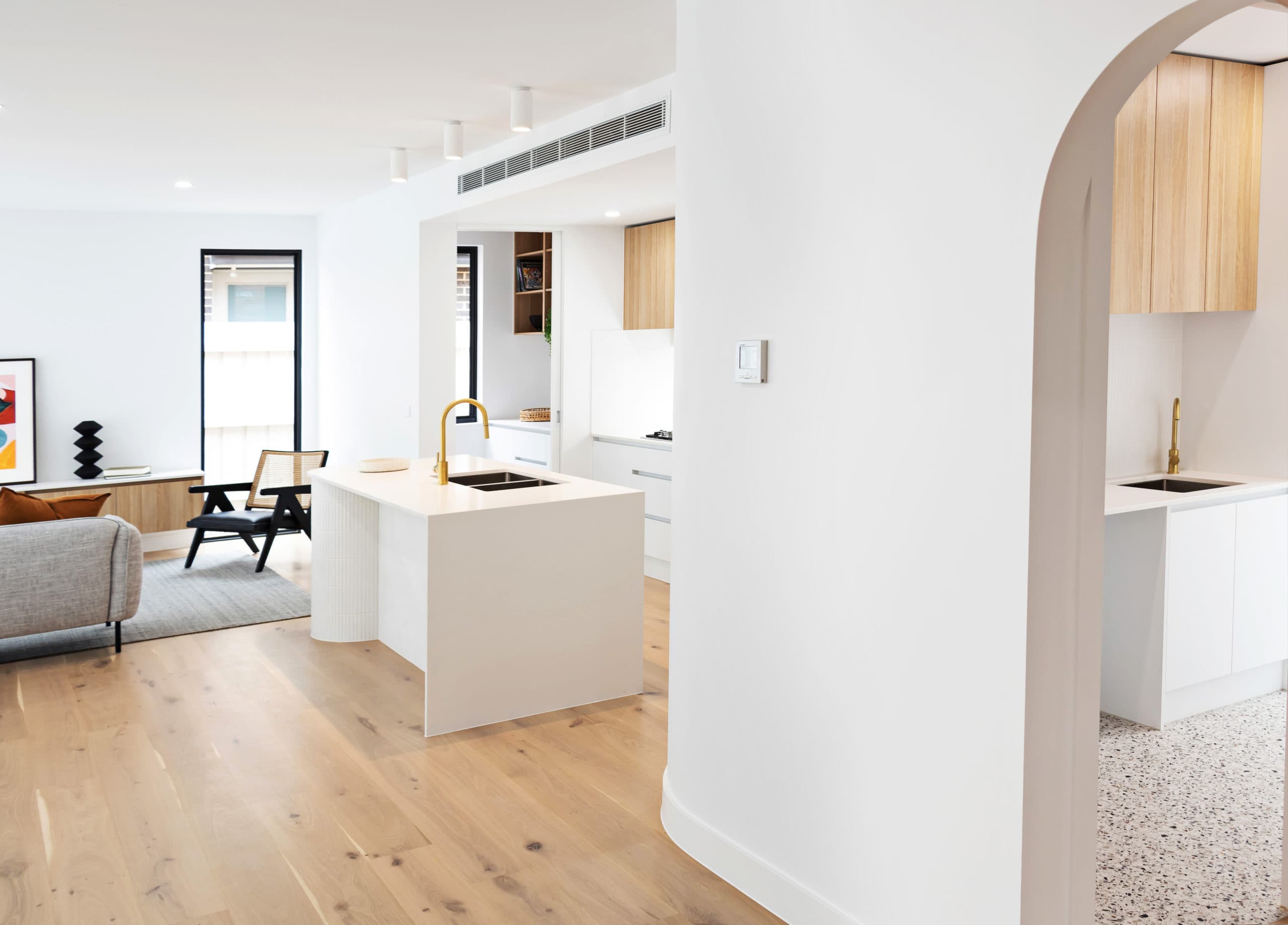 Curved white kitchen island at Groves with brass tapware, seen through an archway