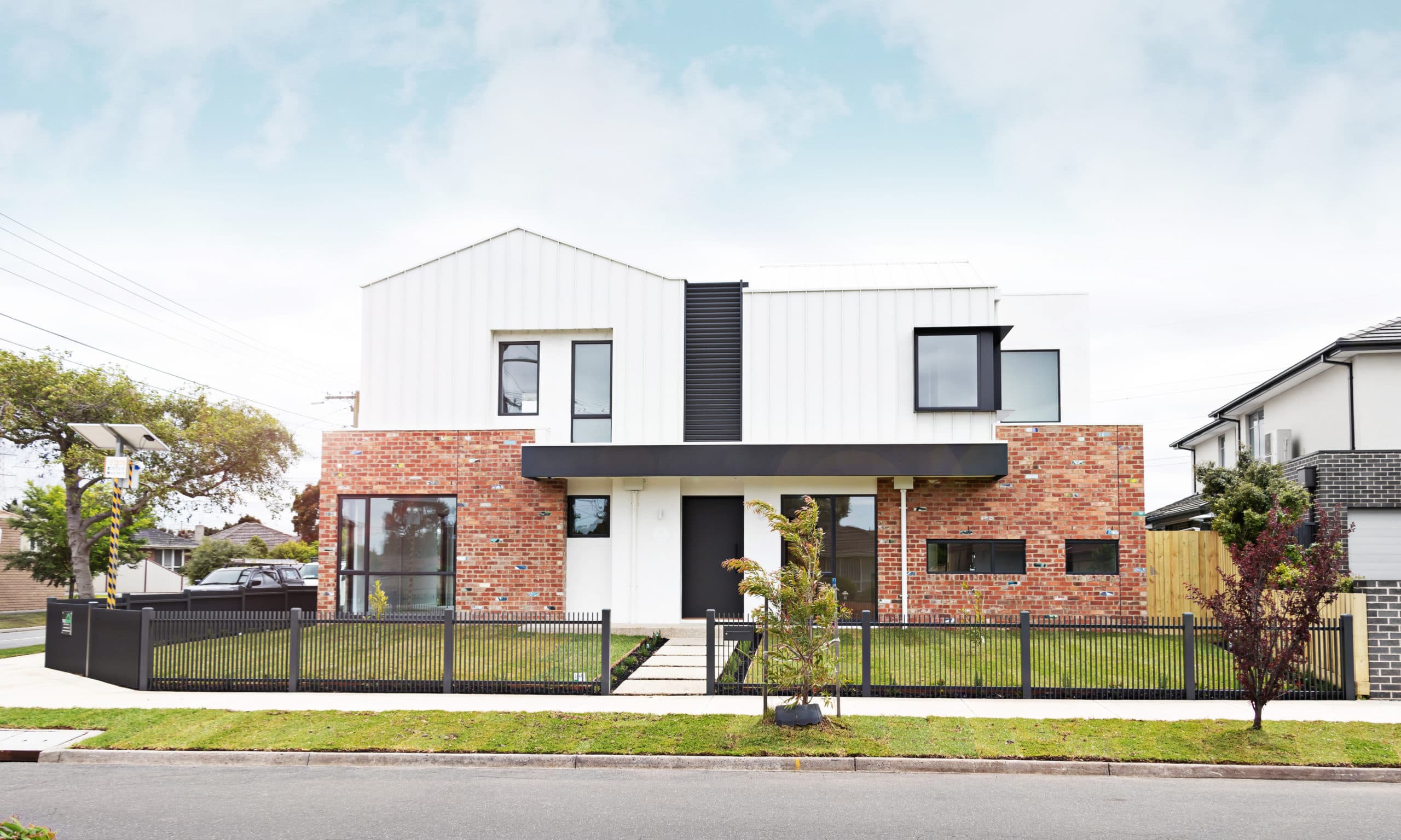 Street facade of Groves in Keilor East: custom white cladding over recycled brick, behind a black picket fence