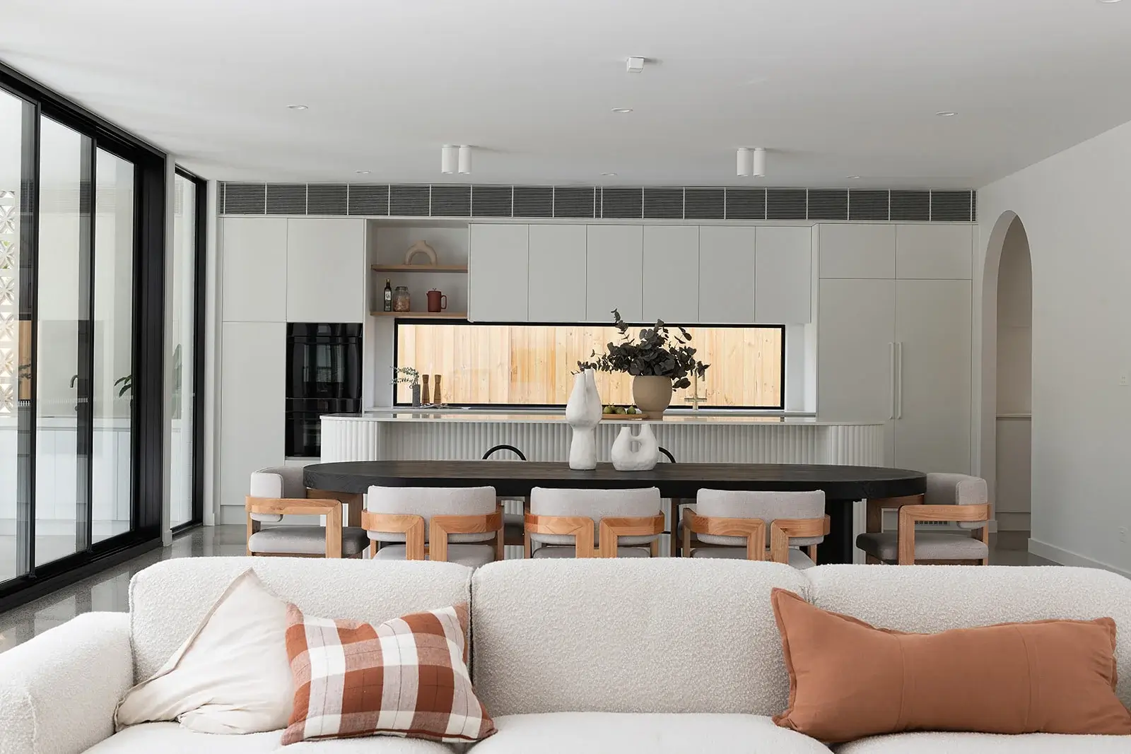 Open-plan living and dining at Patricia, with a curved fluted island bench and timber-framed chairs