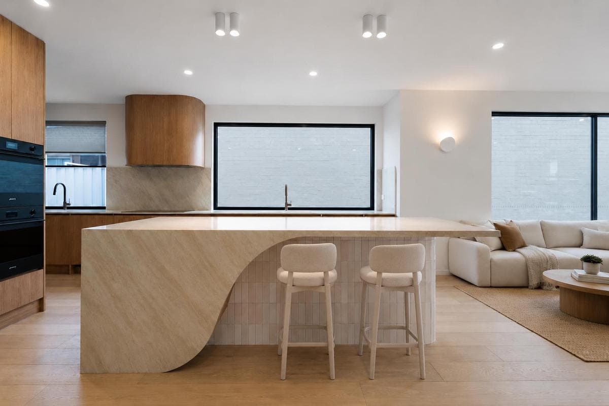 Kitchen at Ridley: a curved Taj Mahal quartzite island with fluted tile base, beneath a curved American oak rangehood