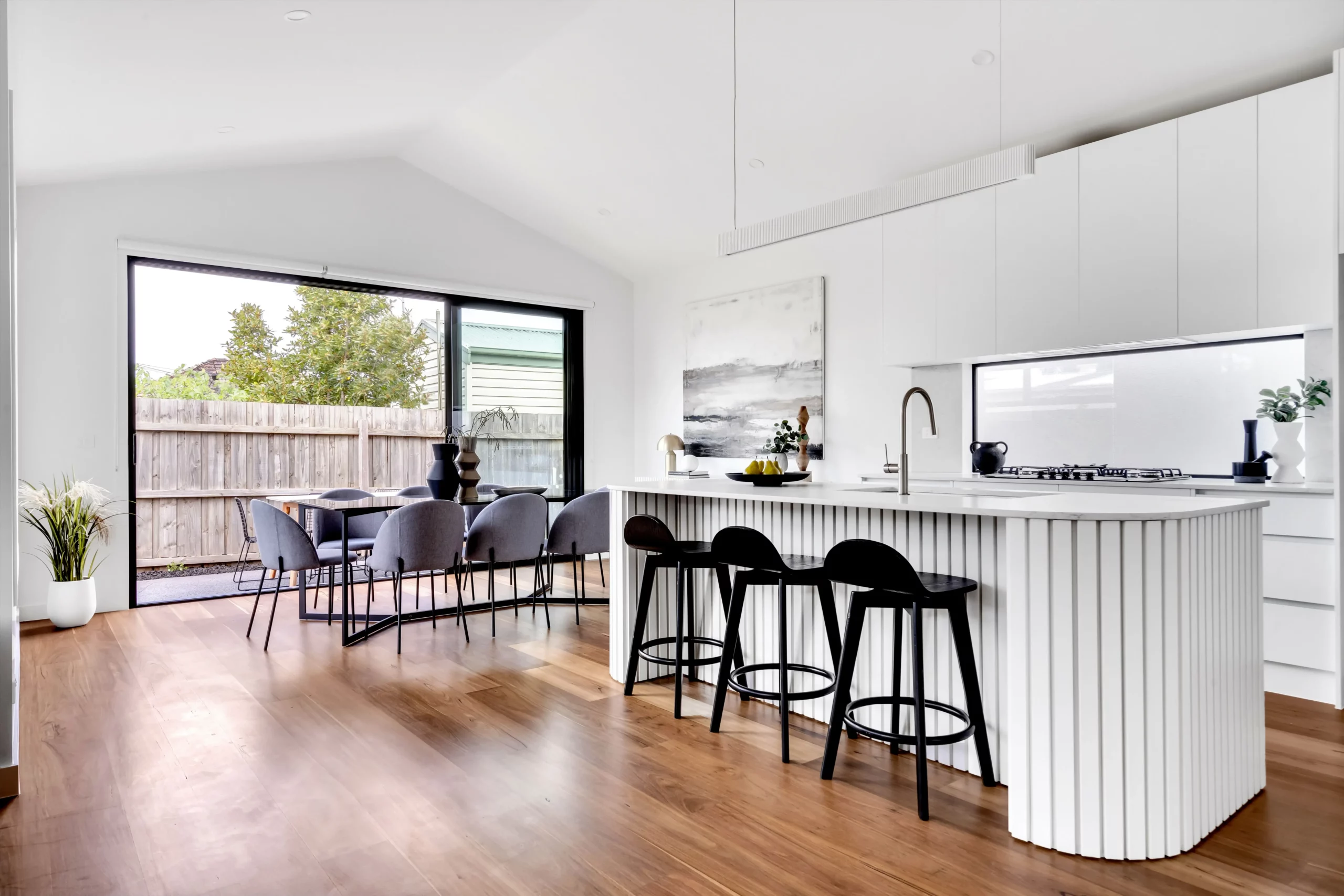 Kitchen and dining at Southbox beneath a raked ceiling, with a fluted island bench and black stools